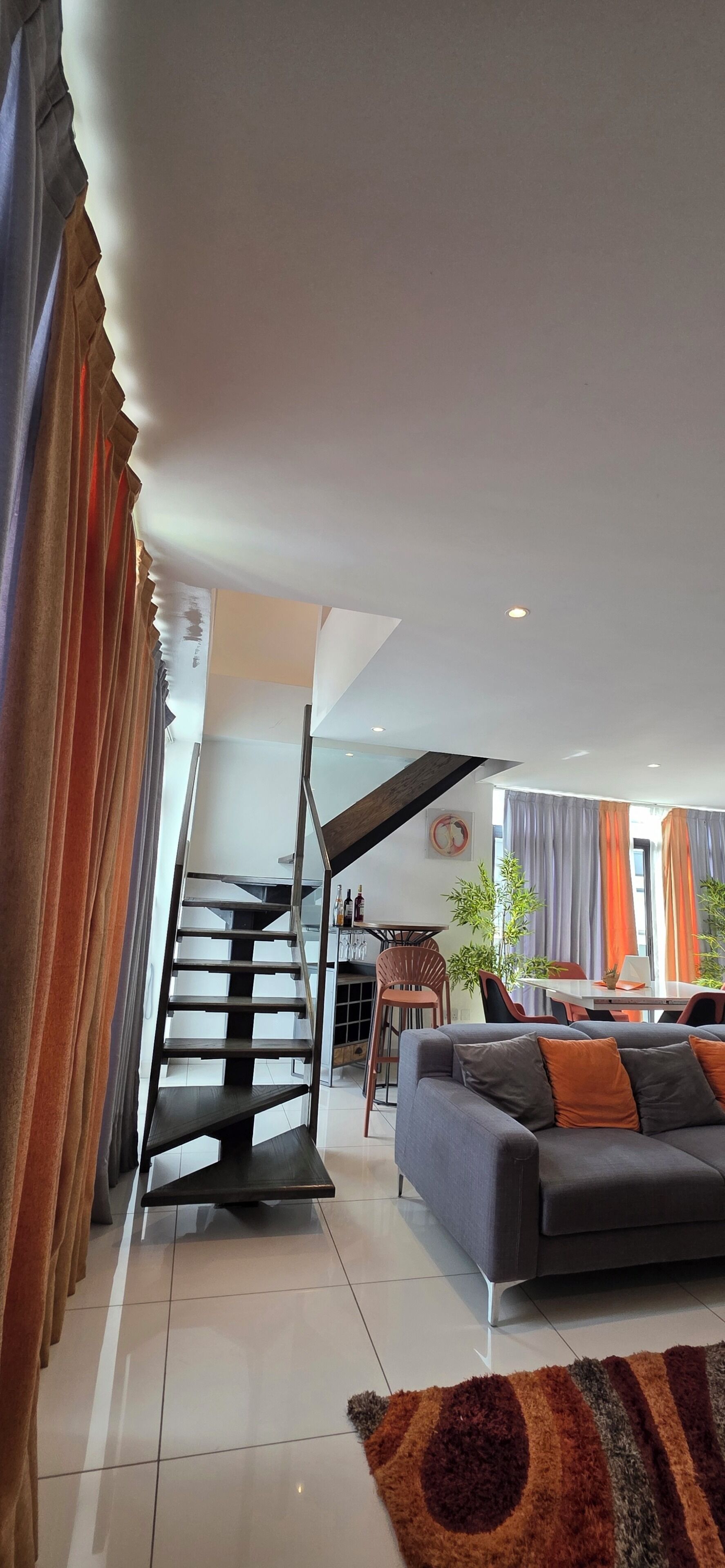 A modern living room with a staircase, a sofa, and a dining area.