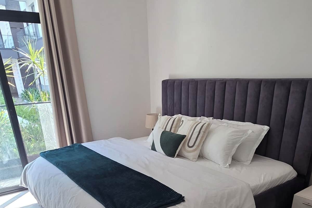 Una habitación de hotel moderna con una cama grande, un cabecero, una mesita de noche y vistas a través de una puerta corrediza de vidrio.