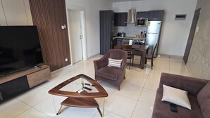 Un salon moderne avec un téléviseur à écran plat, une table basse en verre et deux canapés.
