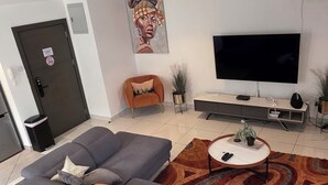 Un salon moderne avec un canapé gris, une table basse ronde, un téléviseur à écran plat et un tapis à motifs.