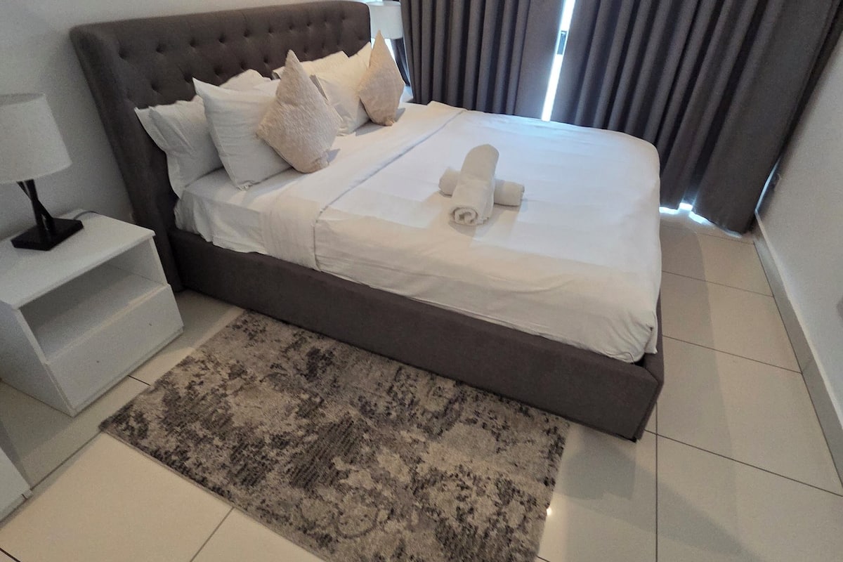 Una habitación de hotel moderna con una cama grande, una mesita de noche, una alfombra y cortinas.