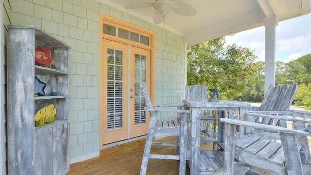 A covered porch with a wooden table and chairs, a white ceiling fan, and a door with glass panels. - Experience Oak Island living in "A Gift From Heaven," a 3BR water view retreat for 6. (Oak Island)