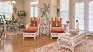 A spacious living room with a dining area, featuring a chandelier, two armchairs with cushions, a side table, and a decorative glass table. - Experience Oak Island living in "A Gift From Heaven," a 3BR water view retreat for 6. (Oak Island)