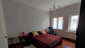 A bedroom with a bed, a chair, a small table, two windows, and a radiator. - Villa glycines spacious 2 bedrooms close to town center enclosed garden dogs ok (Carcassonne)