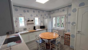 A kitchen with a dining table and chairs, a refrigerator, a microwave, and a window with a view of greenery. - Villa glycines spacious 2 bedrooms close to town center enclosed garden dogs ok (Carcassonne)