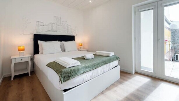 Ein Schlafzimmer mit Bett, Nachttischen, einer Stadtlandschaft als Wandbild und einem großen Fenster.