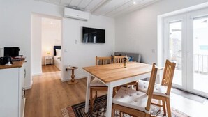 Eine moderne Wohnung mit Holztisch, weißen Wänden, einem flachbildfernseher, der darüber angebracht ist, und einer Glastür zum Balkon.