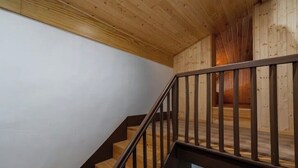 Eine Holztreppe mit Metallgeländer führt zu einem Raum mit weißen Wänden und einer Holzbalkendecke.