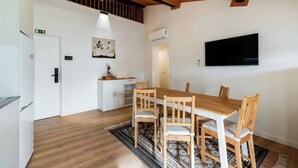Ein Essbereich mit Holztisch und -stühlen, einem weißen, an der Wand befestigten Fernseher und einem gemusterten Teppich.