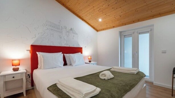 Ein Hotelzimmer mit einem großen Bett, einer Holzbalkendecke, einem Wandgemälde und einem Fenster mit Blick.
