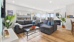Ein modernes Wohnzimmer mit einer Couch, einem Hocker und einem Couchtisch, einem Flachbildfernseher und einem Kamin.