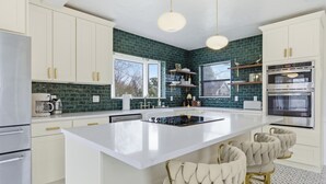 Une cuisine moderne avec des meubles blancs, un grand îlot central et un dosseret recouvert de carreaux verts.