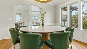 Un coin repas avec une table ronde, des chaises à revêtement vert, un vase rempli de fleurs et un luminaire au plafond au design original.