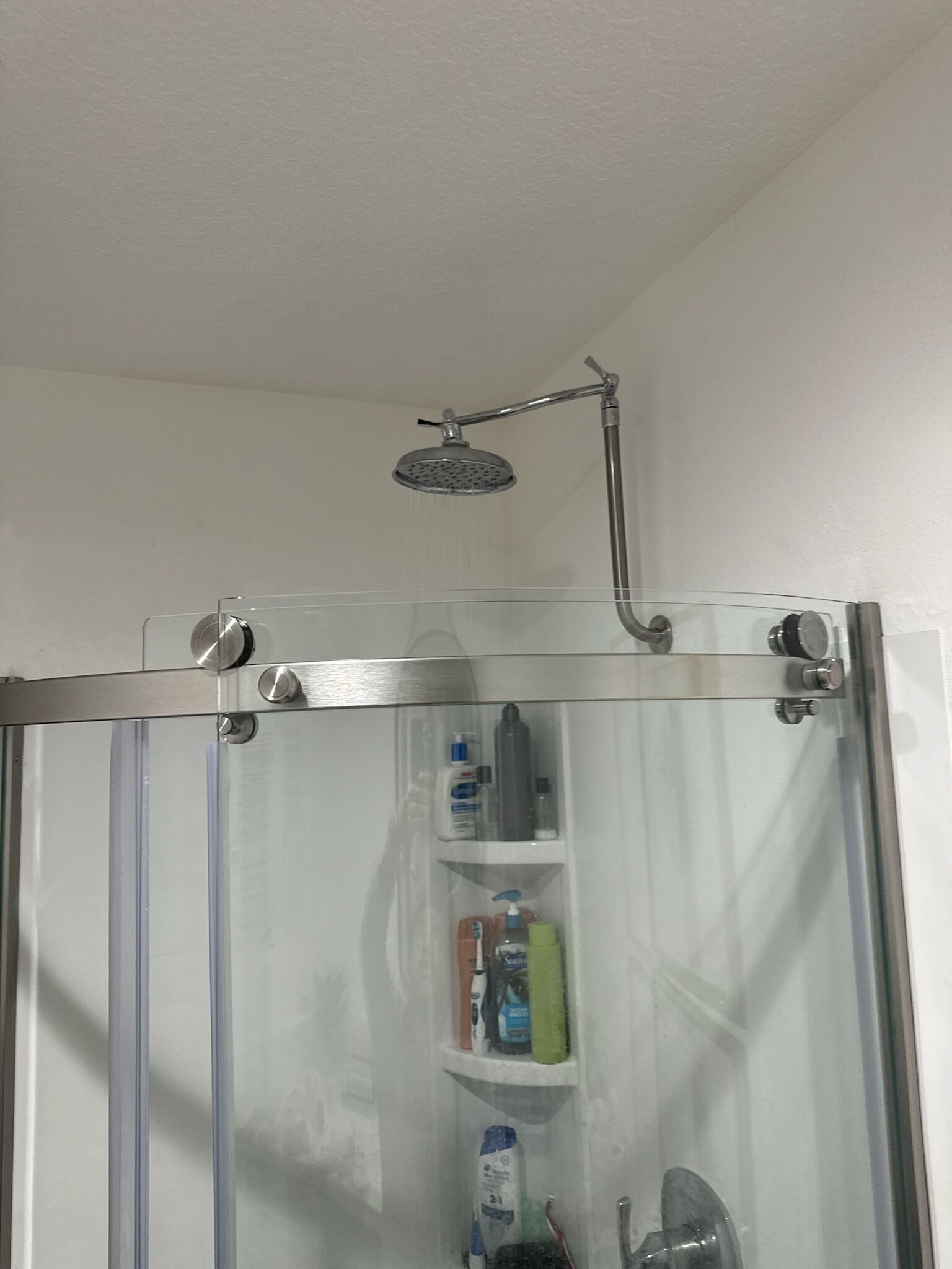 A glass-enclosed shower with a handheld showerhead, a glass door, and a shelf with toiletries.