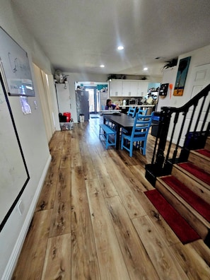Una cocina con suelo de madera, una mesa de comedor con sillas azules y una escalera con alfombra roja.