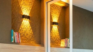 Une chambre d’hôtel équipée d’un lit, de tables de chevet, d’un miroir et d’un système d’éclairage fixé au mur.