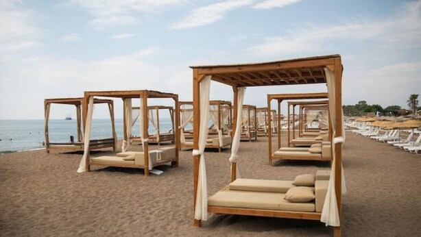 Une plage où des lits de plage dotés de toits en bois sont alignés le long du rivage.
