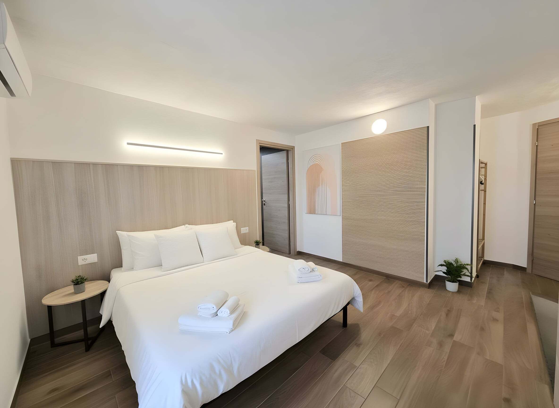 A modern hotel room with a large bed, bedside table, and a small potted plant.