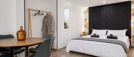 Et moderne værelse med træloft, en seng med hvidt sengetøj, et rundt bord med stole og et knagered med tøj.