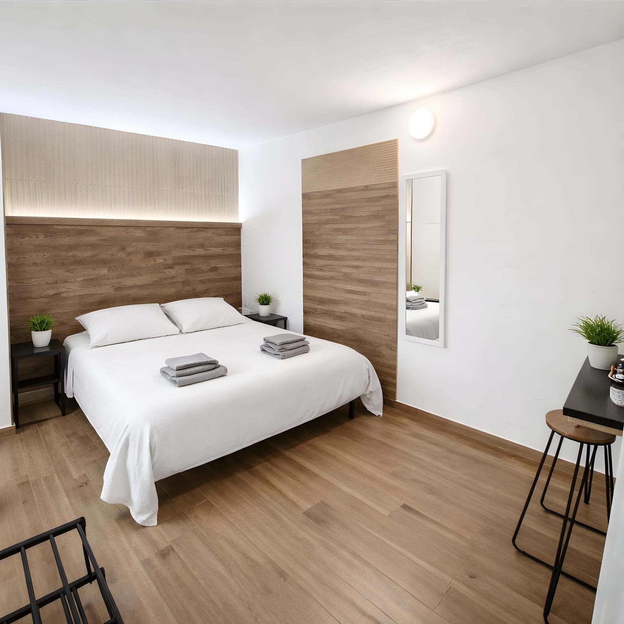 Quarto moderno com uma cama grande, mesas de cabeceira, um espelho e uma pequena escrivaninha com cadeira.