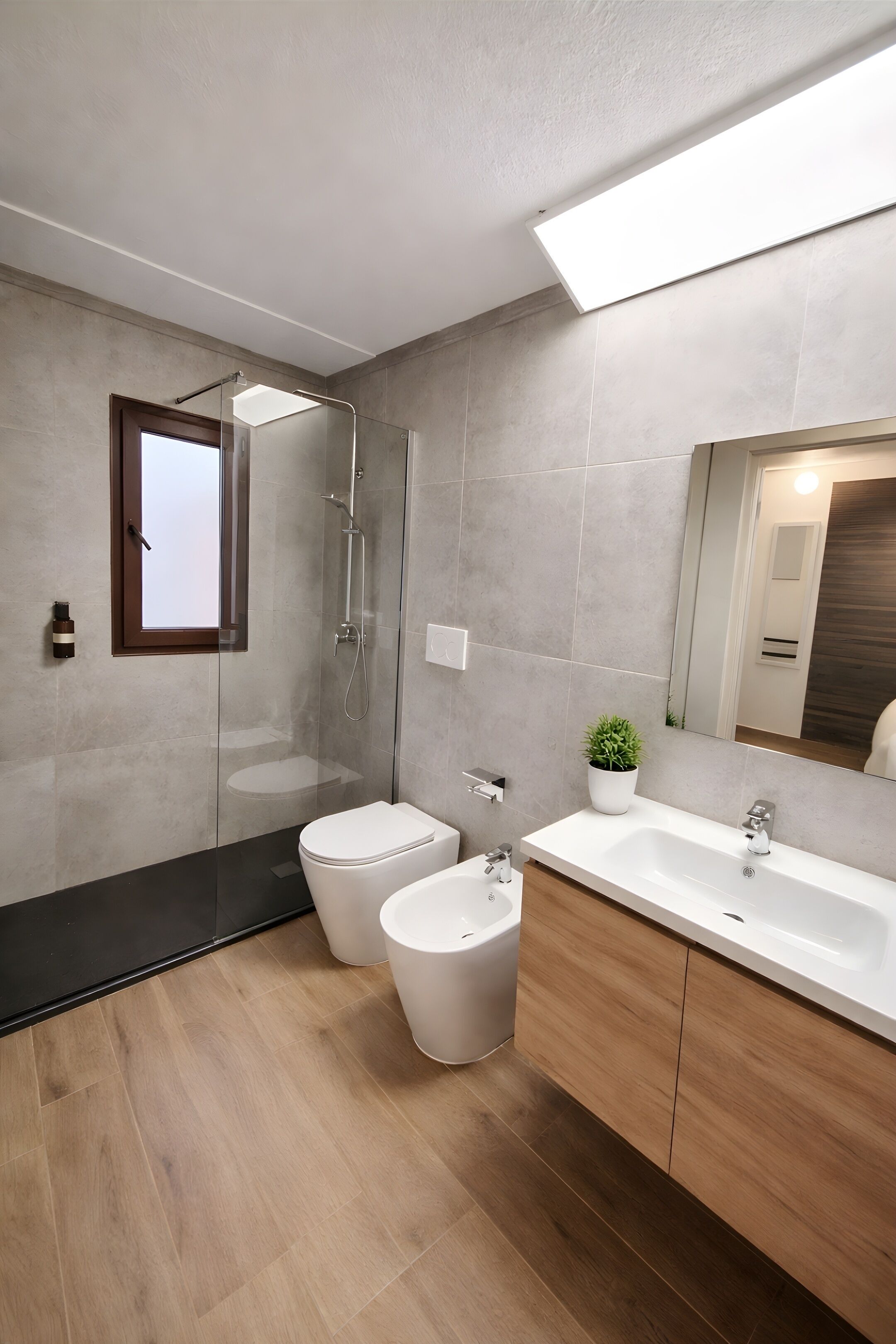 A modern bathroom with a shower, toilet, bidet, and a large mirror.