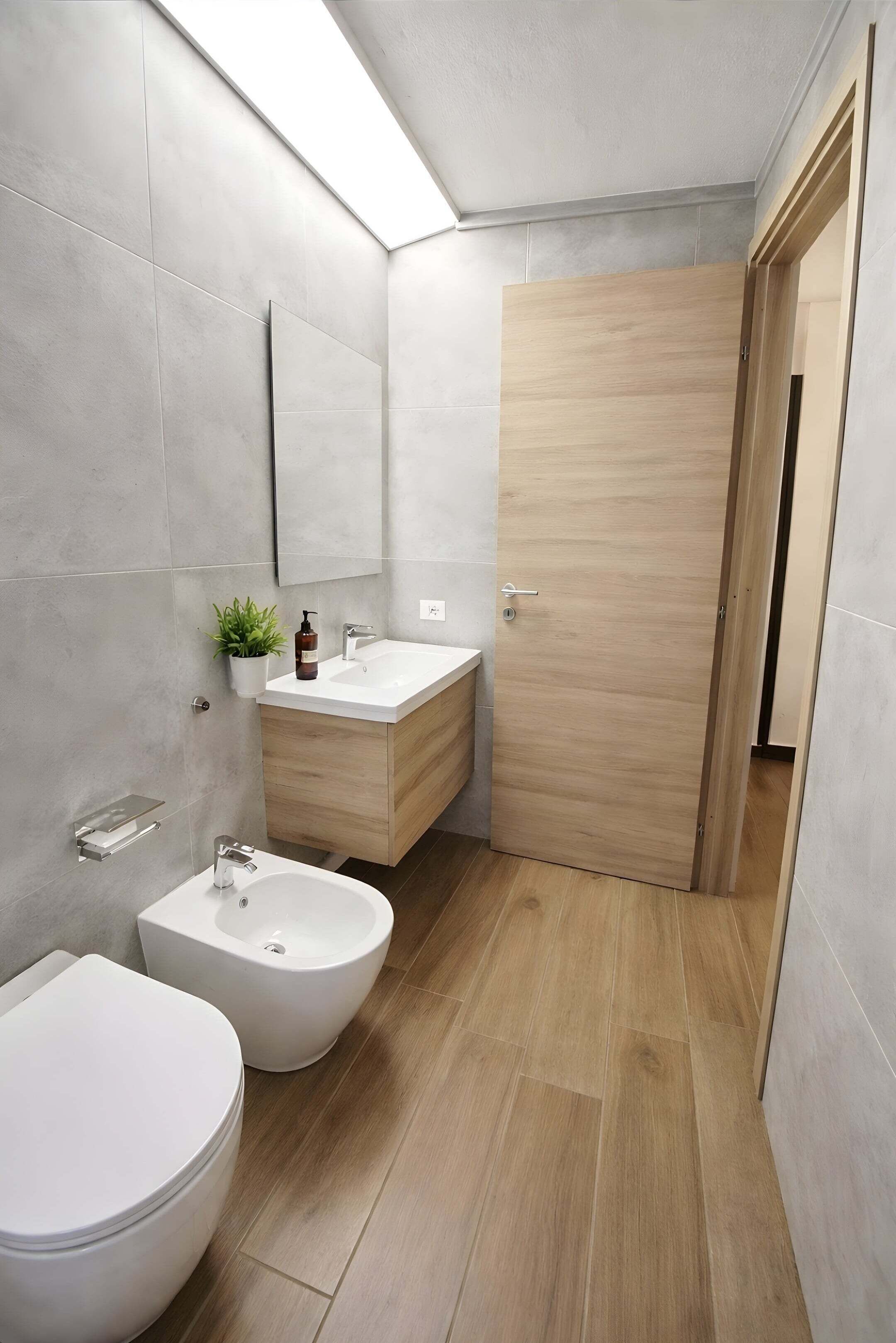 Un baño moderno con inodoro, bidé, tocador y puerta de madera.