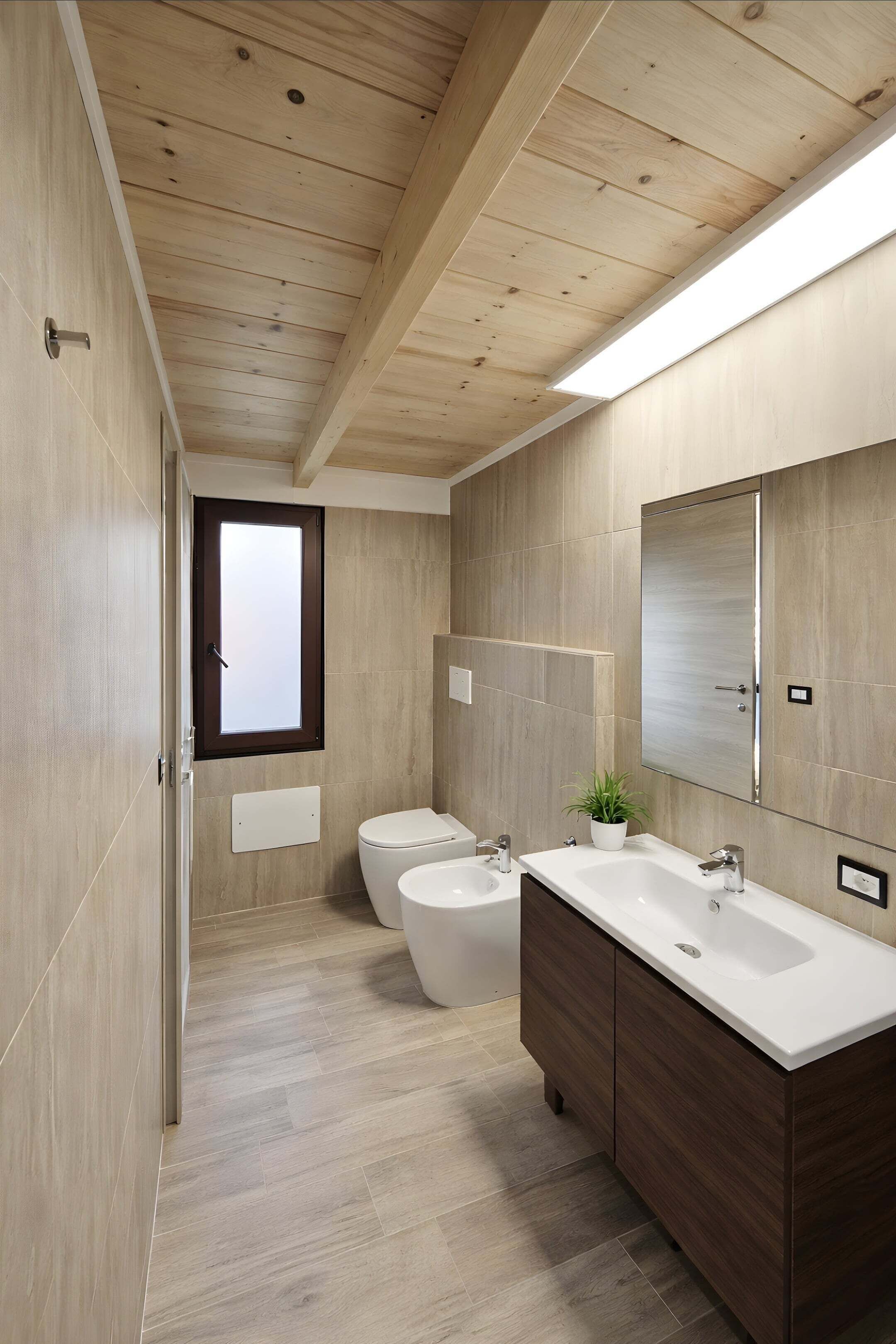 Une salle de bain moderne avec un plafond en bois, deux toilettes, un grand miroir et un meuble-lavabo agrémenté d’une plante.