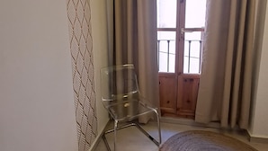 A room with a clear glass chair, a patterned wall, a wooden door, and a round rug. - Nest Style Navas (Granada)