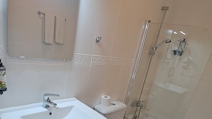 A modern bathroom with a white sink, toilet, and bidet. It features a glass shower enclosure and a wooden floor. - Nest Style Navas (Granada)
