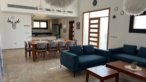 Una sala de estar moderna con comedor, sofás azules, una mesa de centro de madera y una cocina al fondo.