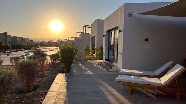 Un edificio moderno con piscina, sillas de descanso y una vista despejada del atardecer.