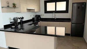 Una cocina moderna con encimera negra, electrodomésticos de acero inoxidable y una ventana sobre el fregadero.
