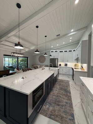 A modern kitchen with a large island, pendant lighting, and a view to the outdoors. - Skyline Tides- Gulf Access -Views -Heated Pool (Cape Coral)