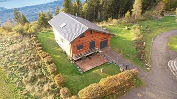 Une cabane dotée d’une terrasse, entourée d’une pelouse bien entretenue et d’une forêt dense.