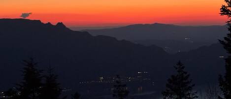 A mountain landscape at dusk with a clear view of the horizon and distant lights.