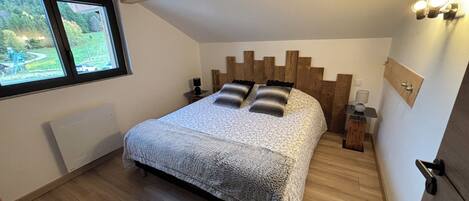 Une chambre à coucher avec un lit, une tête de lit en bois, des tables de chevet, une fenêtre et une vue sur la verdure à l’extérieur.