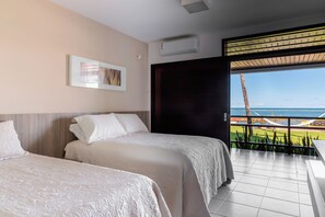 A hotel room with two beds, a large window with a view of the ocean, and an air conditioning unit.