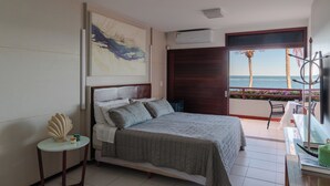 A bedroom with a bed, a small table, a decorative shell, a painting, an air conditioner, and a balcony with a view of the sea. - Casa Manaua: beachfront property with incredible views in Barra de São Miguel (Barra de São Miguel)