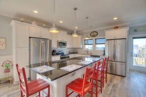 A modern kitchen with white cabinetry, stainless steel appliances, and red bar stools. - Inn Shore You: Ocean View Home, Private Pool, Putting Green (Oak Island)