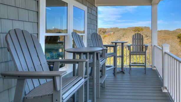 Eine überdachte Veranda mit Adirondack-Stühlen und Tischen, mit Blick auf eine natürliche Landschaft.