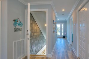 A hallway with a staircase, a welcome sign, and a bicycle decoration. - Inn Shore You: Ocean View Home, Private Pool, Putting Green (Oak Island)