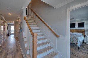 A staircase with wooden handrails leading to a bedroom with a bed and a headboard. - Inn Shore You: Ocean View Home, Private Pool, Putting Green (Oak Island)