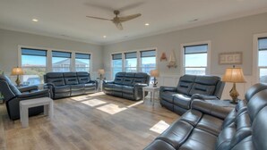 Ein geräumiges Wohnzimmer mit Ledersofas, einem Deckenventilator und großen Fenstern mit Blick auf die Stadt.