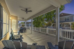 A covered outdoor deck with seating, a ceiling fan, and a view of neighboring houses.