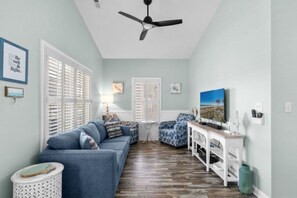 Ein Wohnzimmer mit einem blauen Sofa, einem weißen Beistelltisch, einem Deckenventilator und einem Gemälde an der Wand.