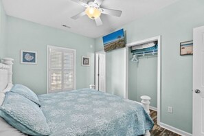 A bedroom with a bed, a ceiling fan, a door, and a wall with a picture.