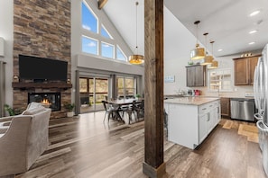 A spacious living area with a fireplace, a dining table, and a kitchen with modern appliances. - Beautiful Views! Hot Tub! Ping Pong! (Branson)