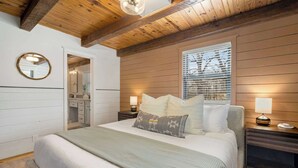 Ein Schlafzimmer mit Bett, Nachttischlampen, einem Spiegel und einem Fenster mit Jalousien.