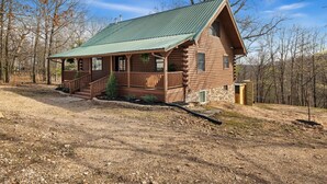 Eine Blockhütte mit einem grünen Metalldach, einer Veranda mit Geländer und einem Steinfundament.