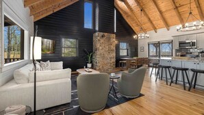Ein modernes Interieur mit einer Steinsäule, einer weißen Couch, grauen Sesseln, einer Küchenzeile und einem Esstisch.